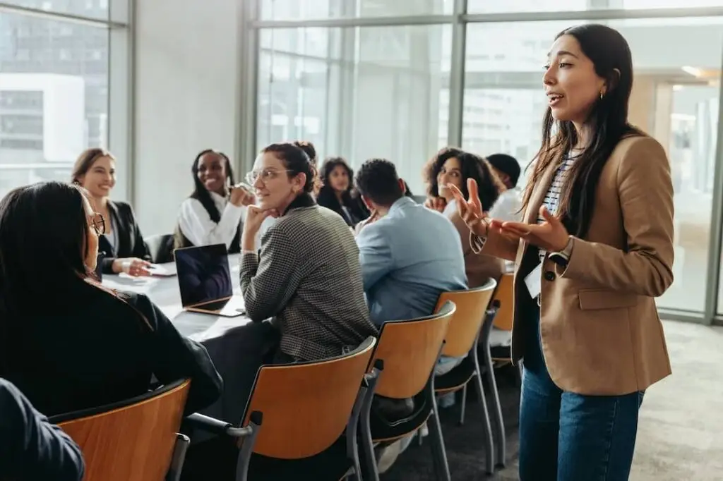 A confident female leader engages a diverse team in a professional workshop, promoting teamwork and fresh ideas in a bright office environment.